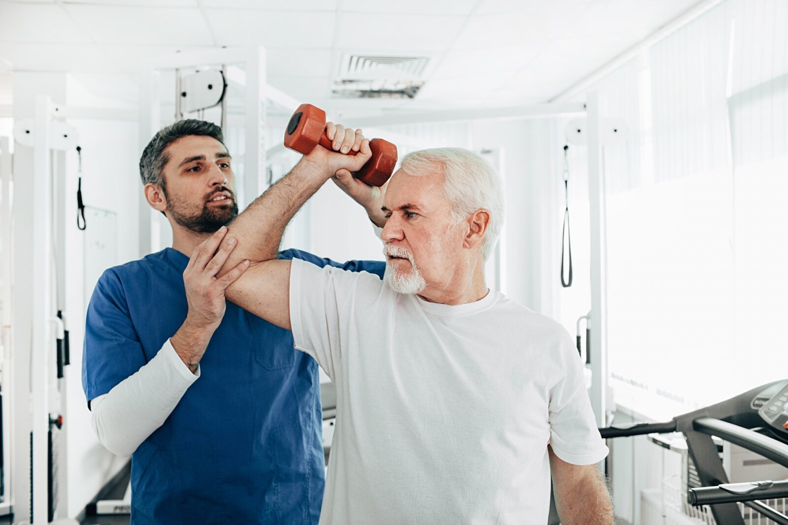 senior man lift a dumbbell, he doing treatment exercise with his physiotherapist. Physio treatment