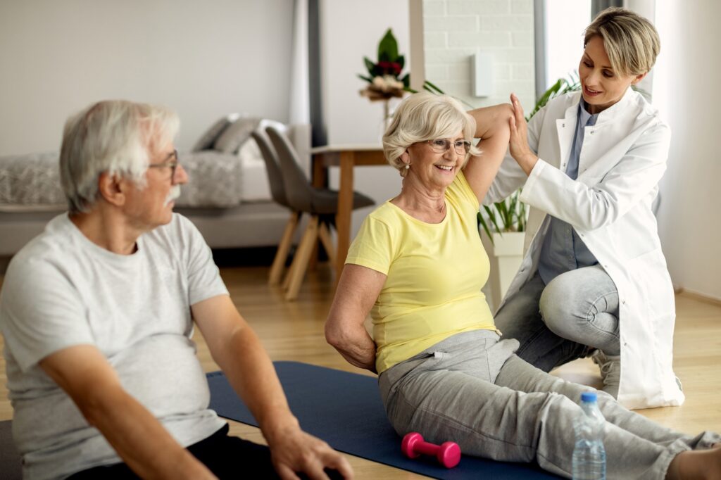 Mature couple exercising with help of physiotherapist at home.