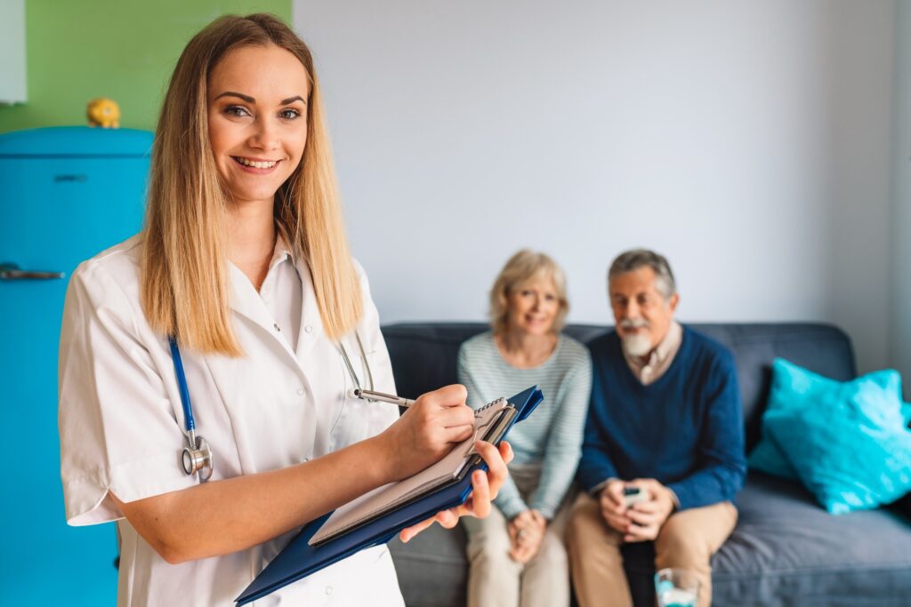 Smiling nurse looking at the camera, holding a notepad while visiting senior couple at nursing home