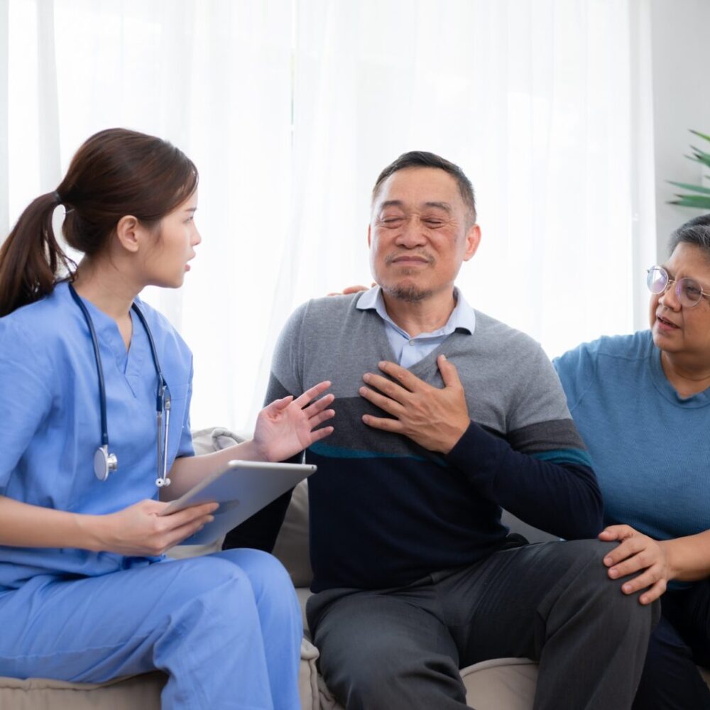 Asian senior patient talking with doctor and nurse on sofa at home