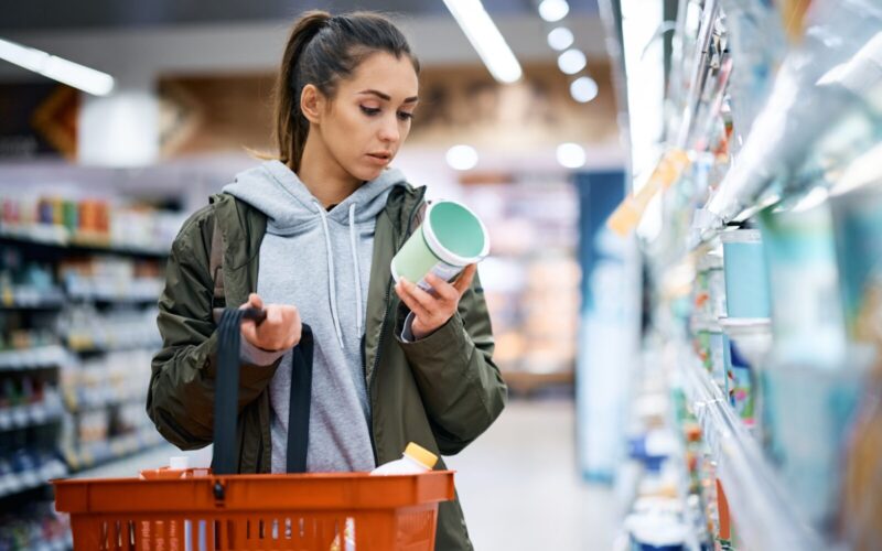 Young woman reading nutrition label while buying diary product in supermarket.